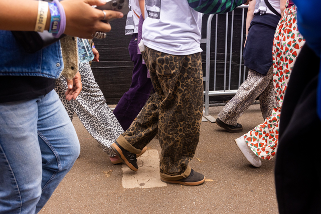 Several people walk on a paved surface wearing colorful patterned pants, including leopard, strawberry, and animal print designs.